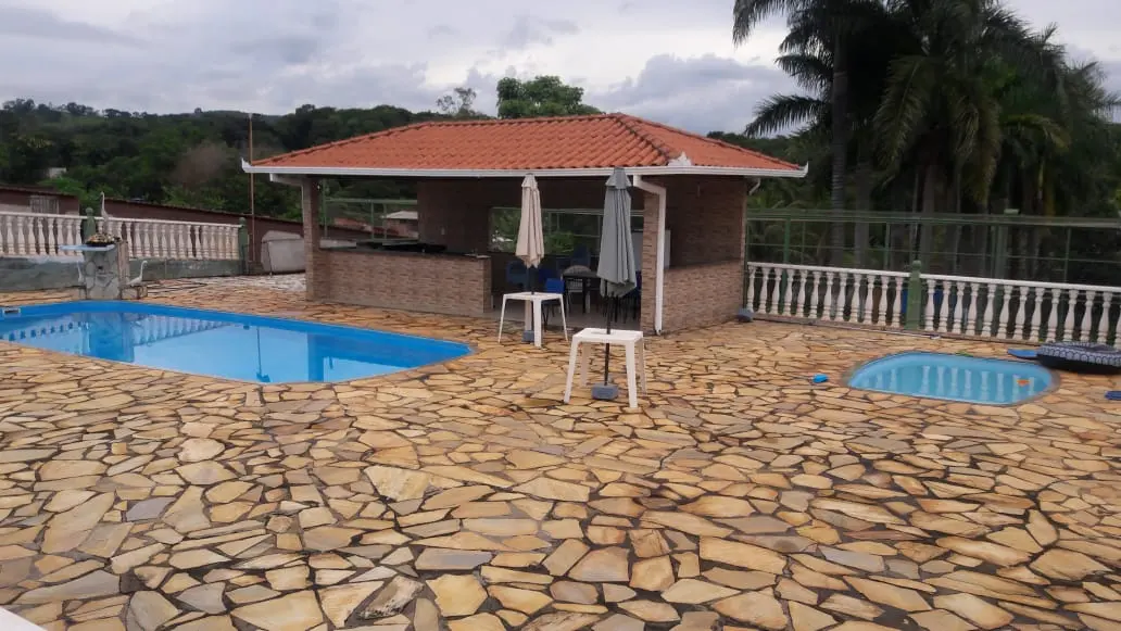 Piscina com deck de pedra e quiosque coberto ao fundo.