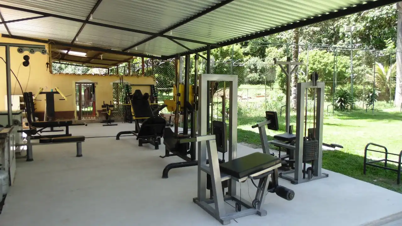Área coberta com aparelhos de musculação, aberta para o gramado.